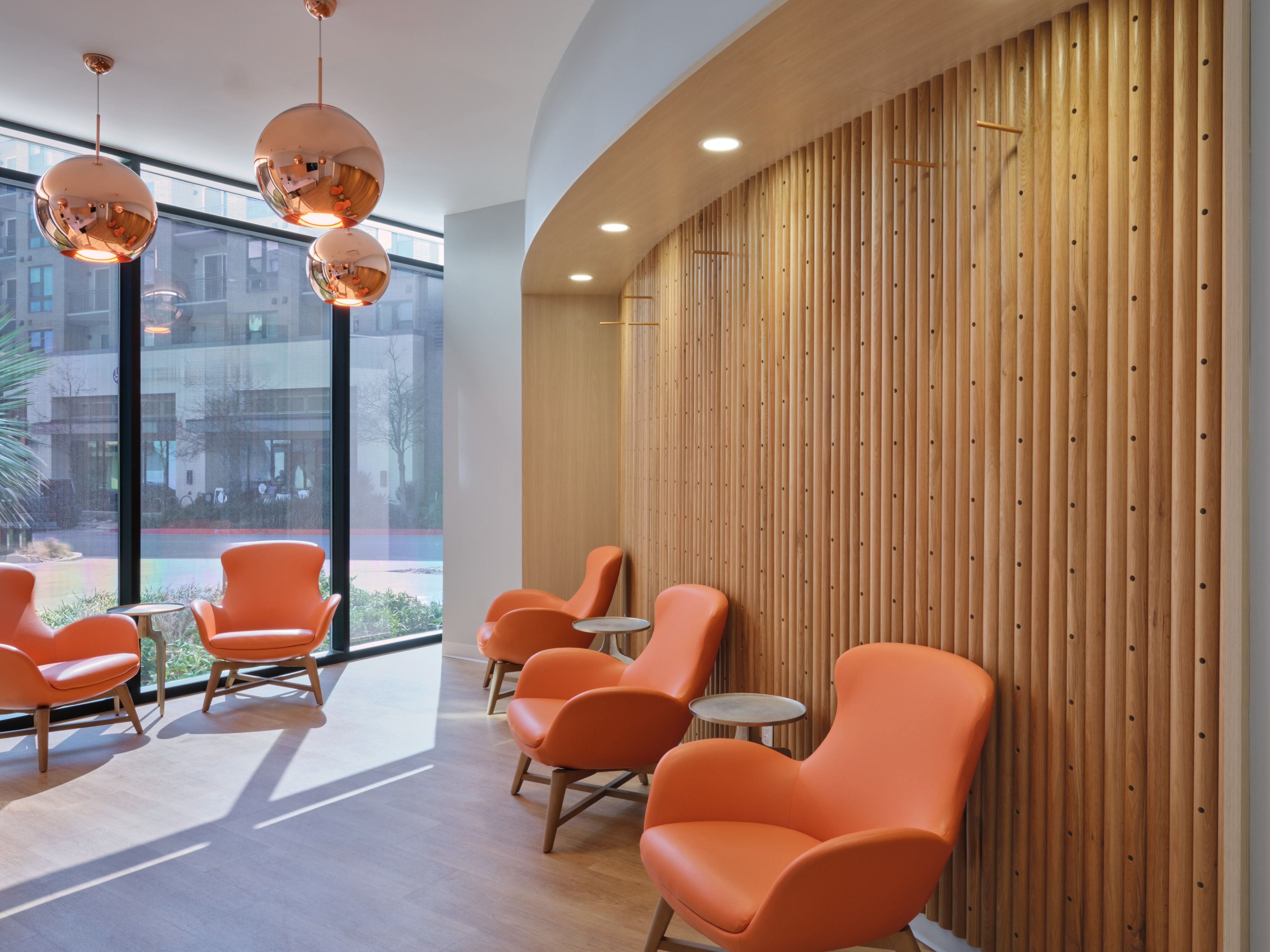 Sunlit lobby with copper pendant lights and orange lounge chairs against a slatted wood wall