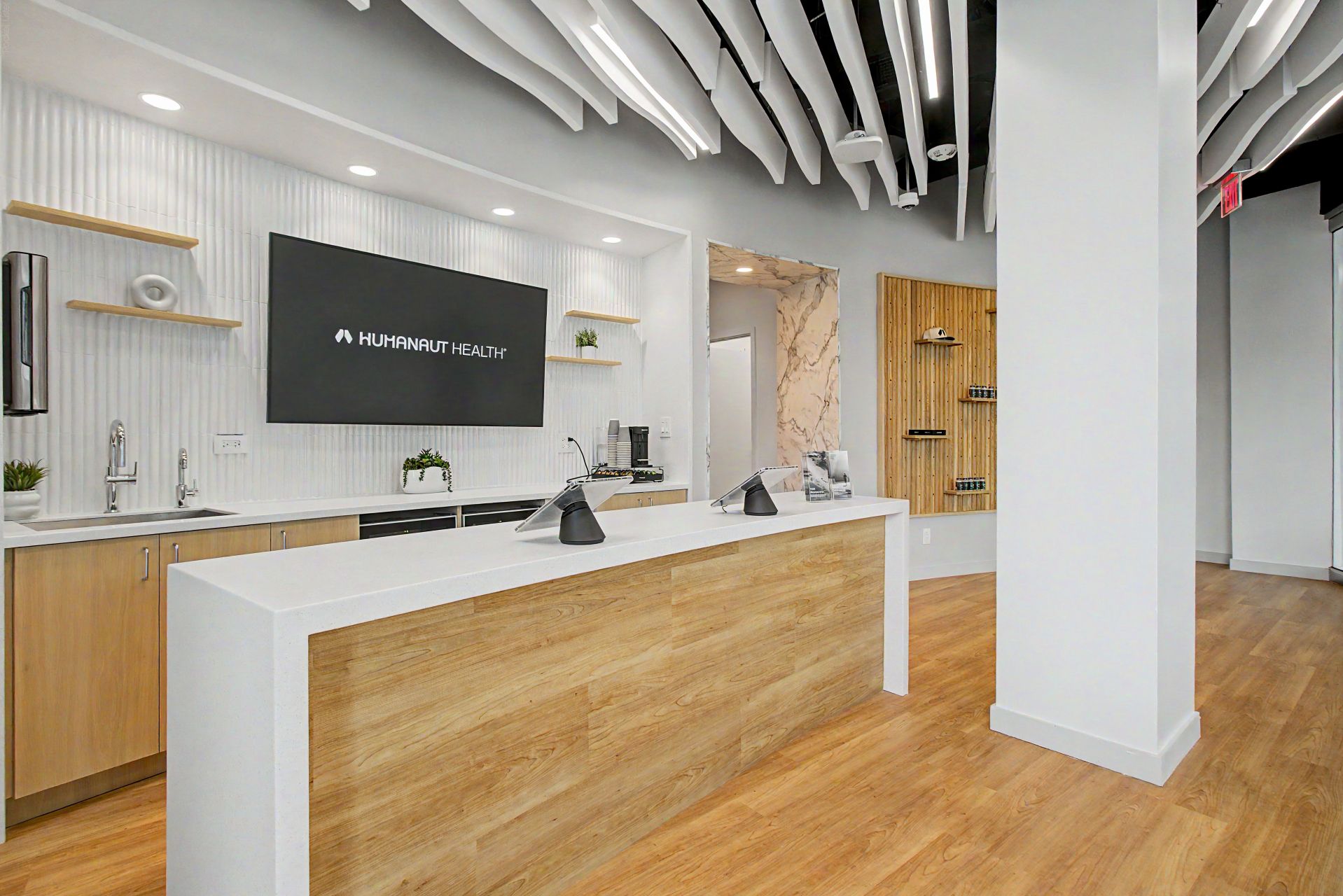 Reception desk with Humanaut Health display and curved ceiling baffles in the Dallas clinic