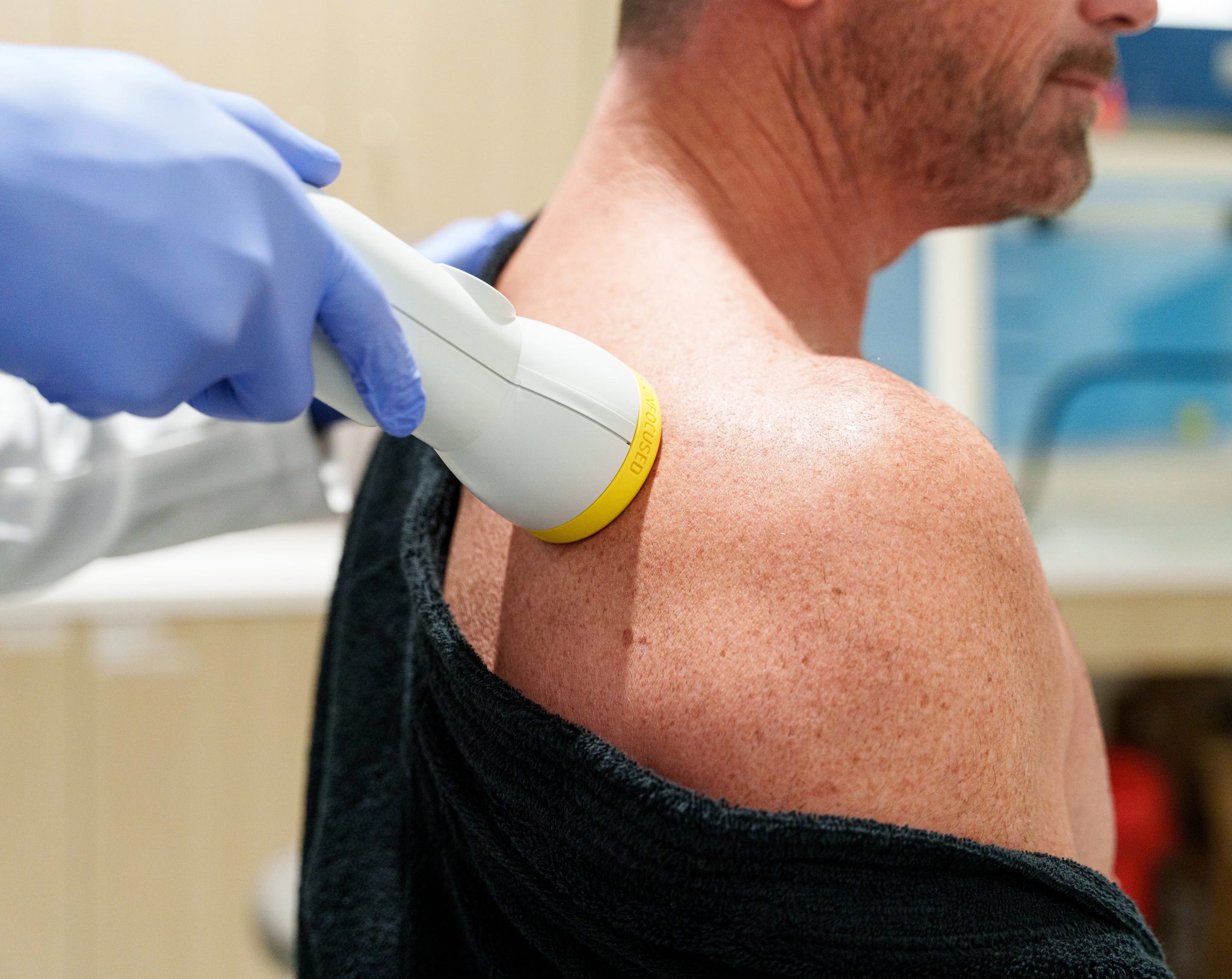 A practitioner applying shockwave therapy to a patient's shoulder