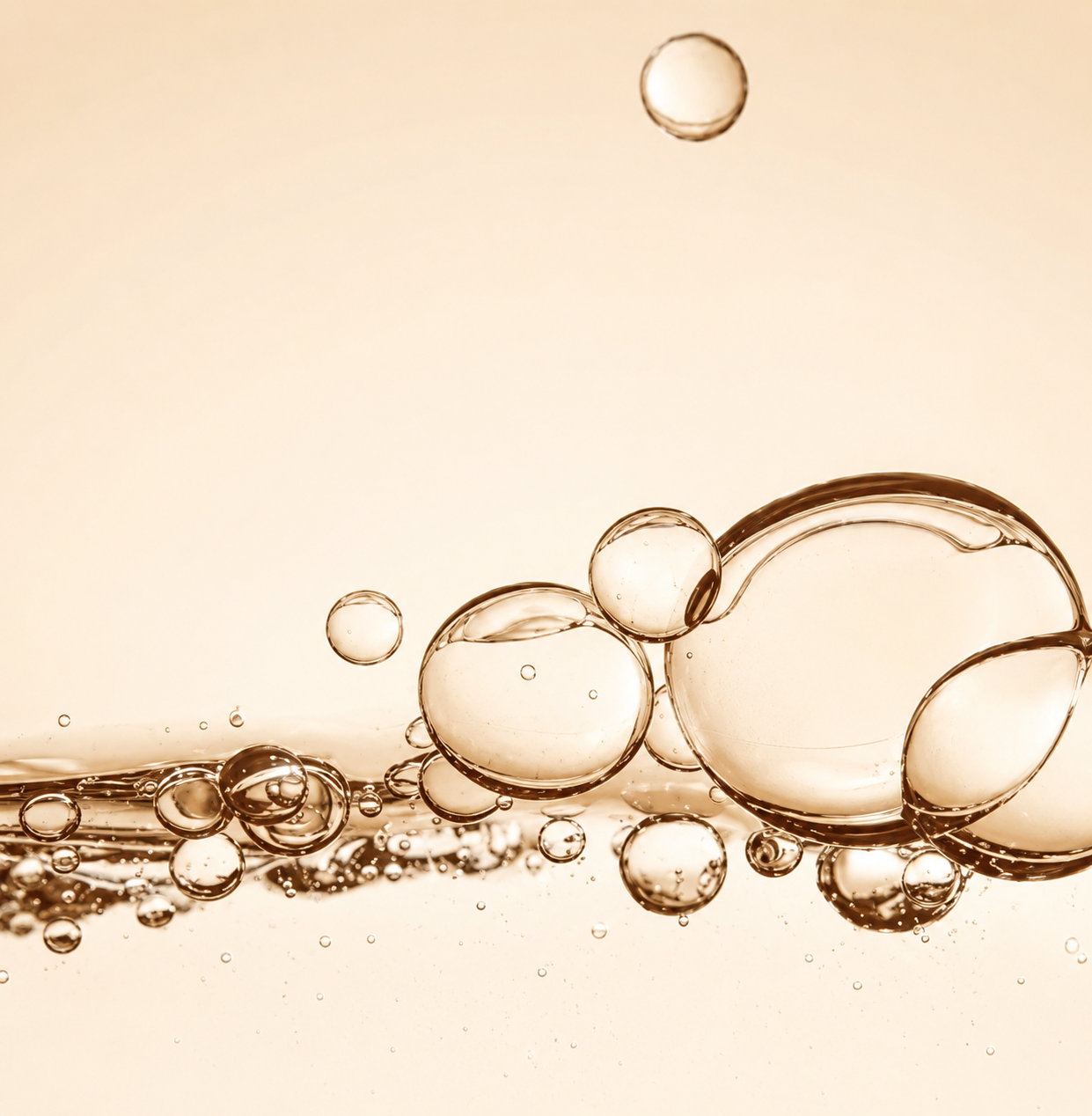 Cluster of crystalline oil bubbles floating in soft beige liquid