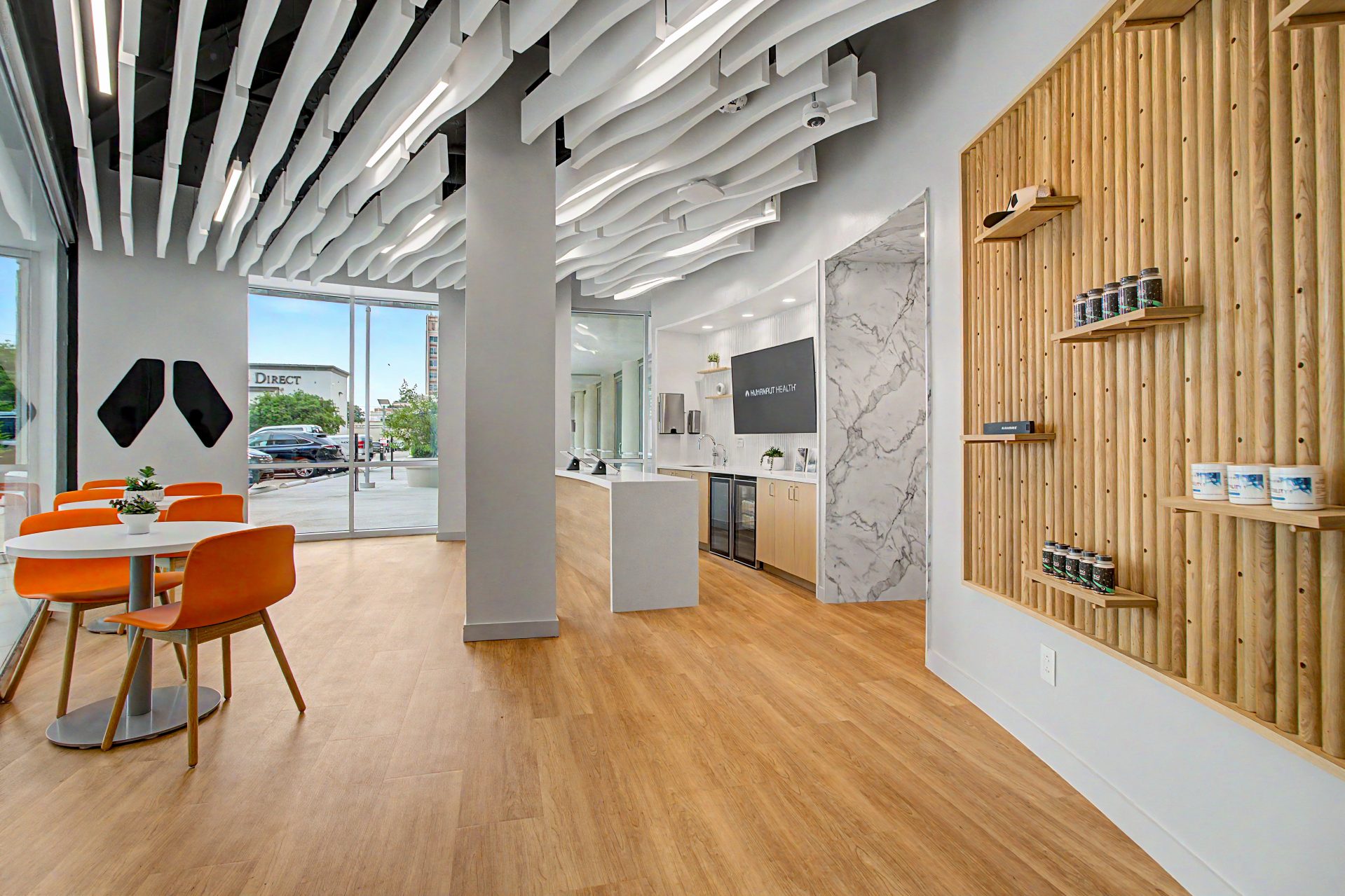 Member lounge with orange chairs, a slatted-wood product wall, and curved ceiling baffles
