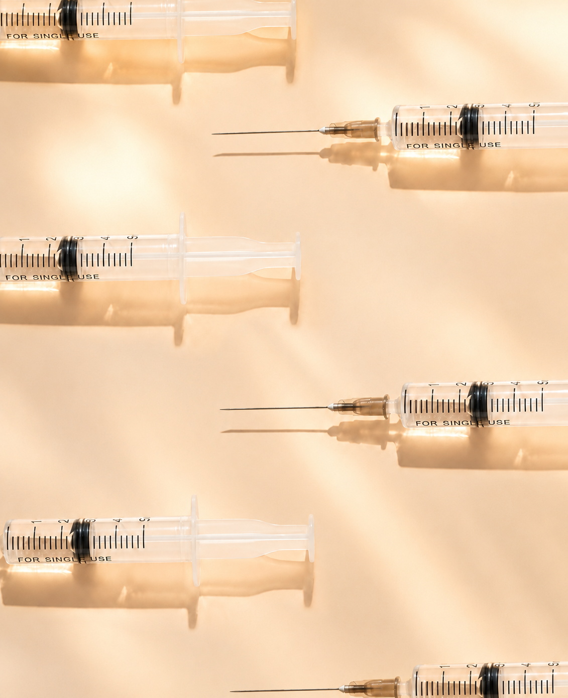 Capped intramuscular syringes lined up against a warm beige background