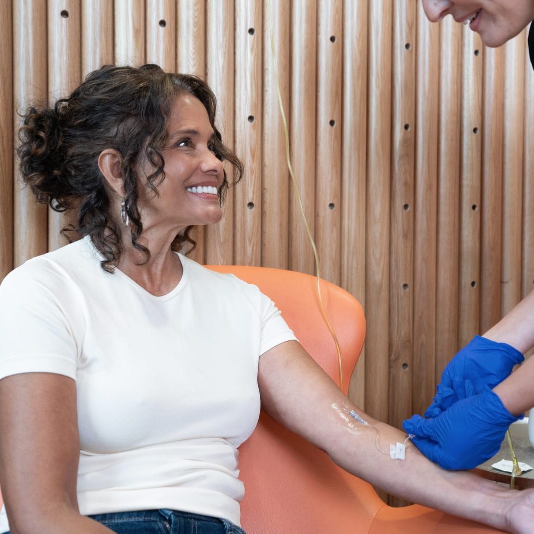 Registered nurse administering an IV infusion to a smiling patient in a clinic chair