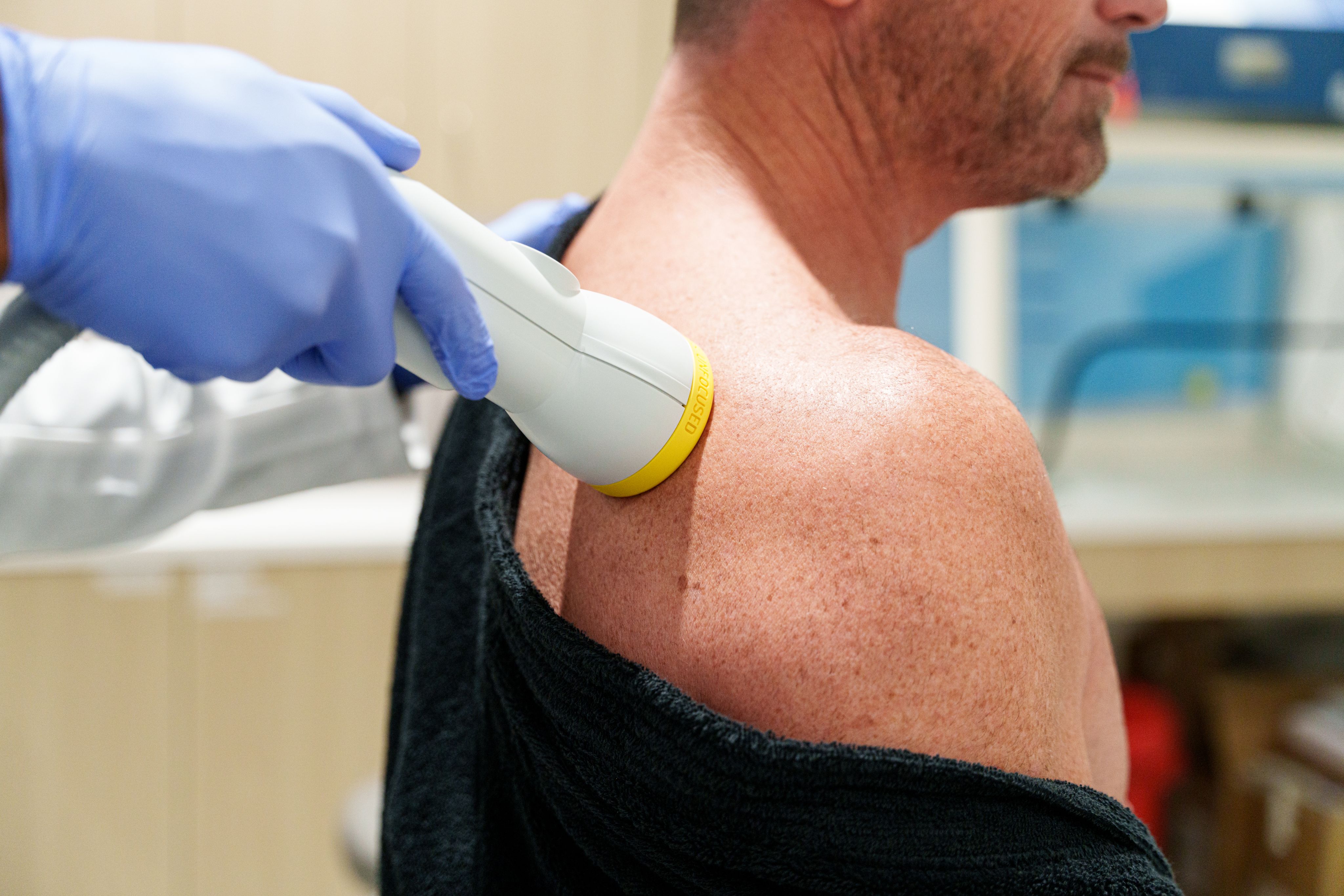 A practitioner applying a shockwave therapy device to a patient's shoulder