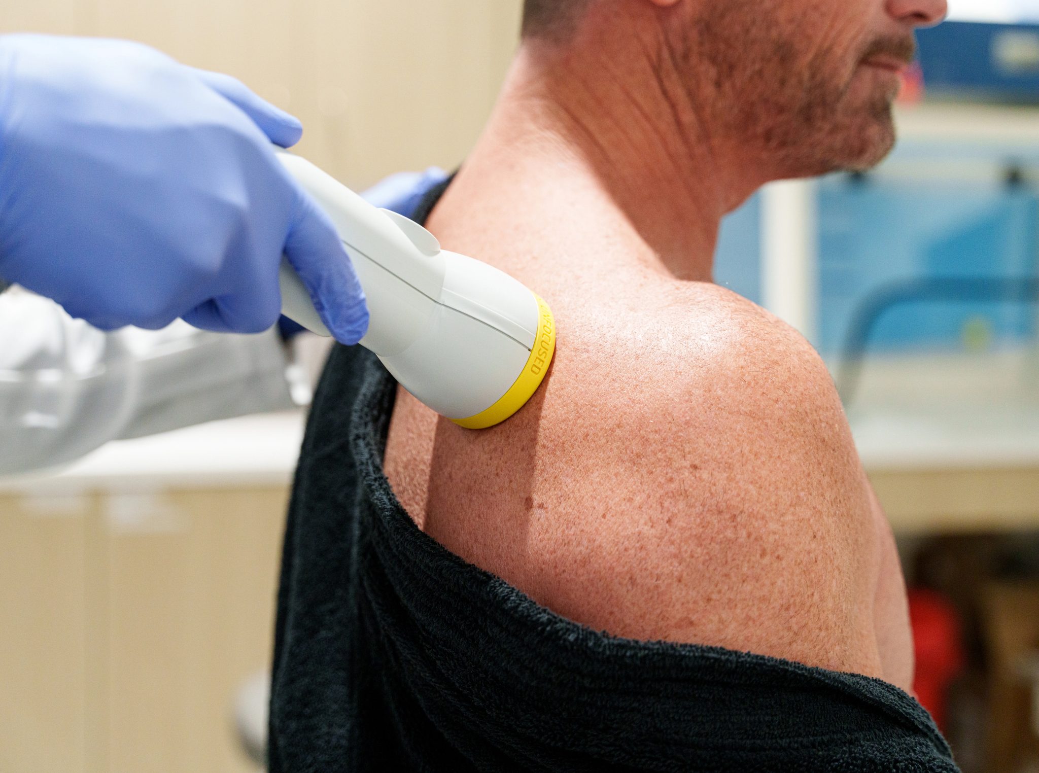 A practitioner applying a shockwave therapy device to a patient's shoulder